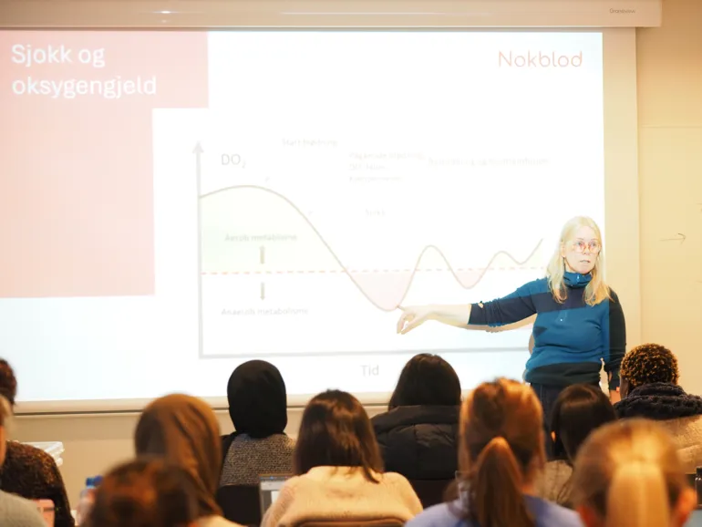 A woman in a classroom pointing at a projector screen