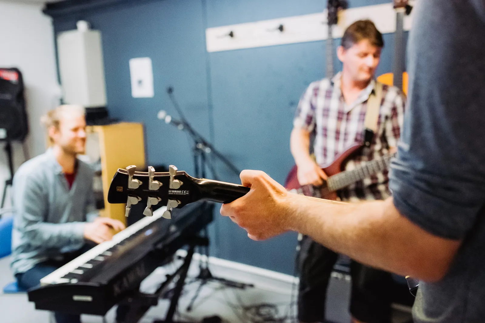 Bilde av en mann som spiller keyboard og to som spiller gitar