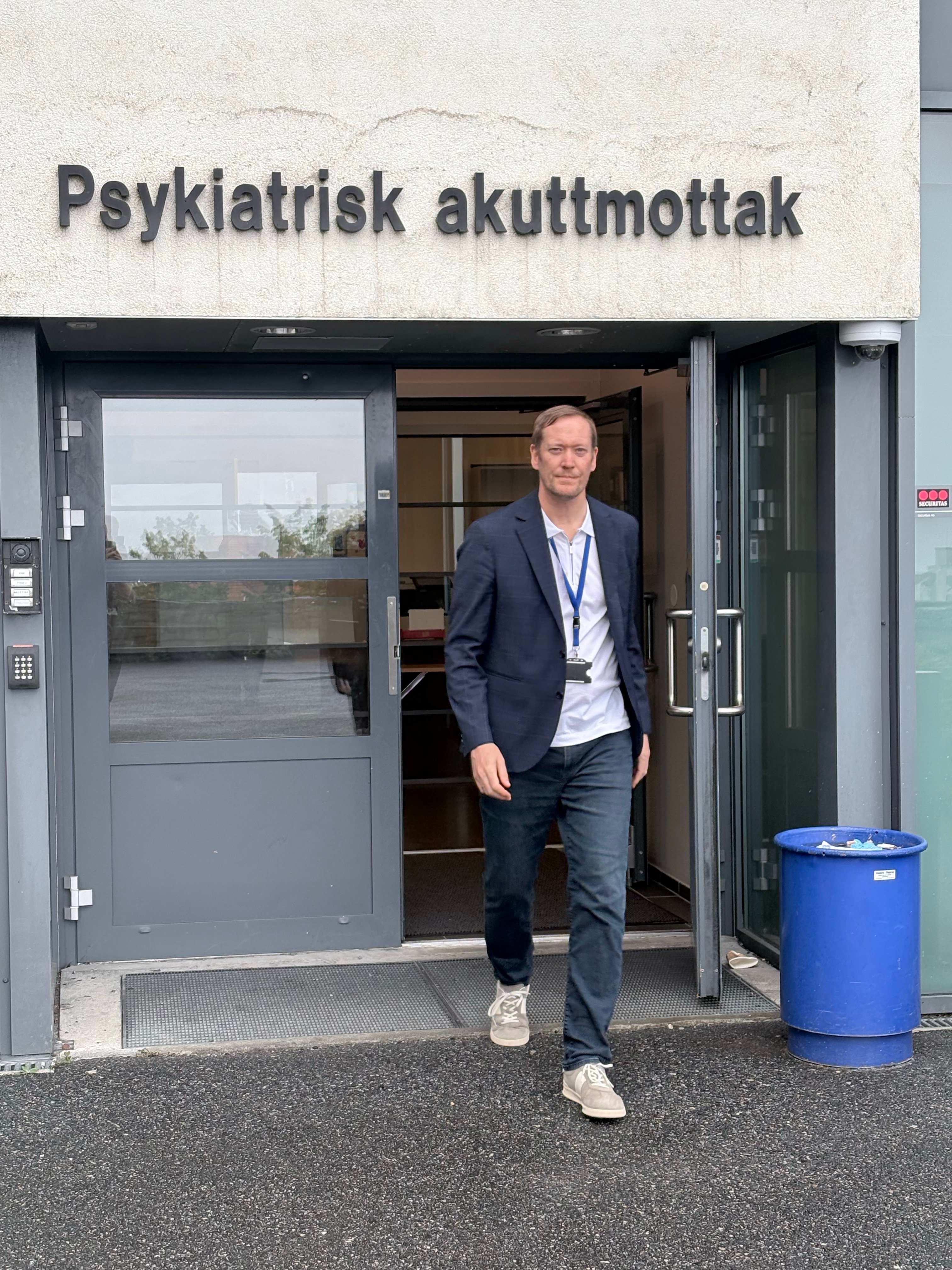 En mann som står ved siden av en inngangsdør som er skiltet med Psykiatrisk klinikk
