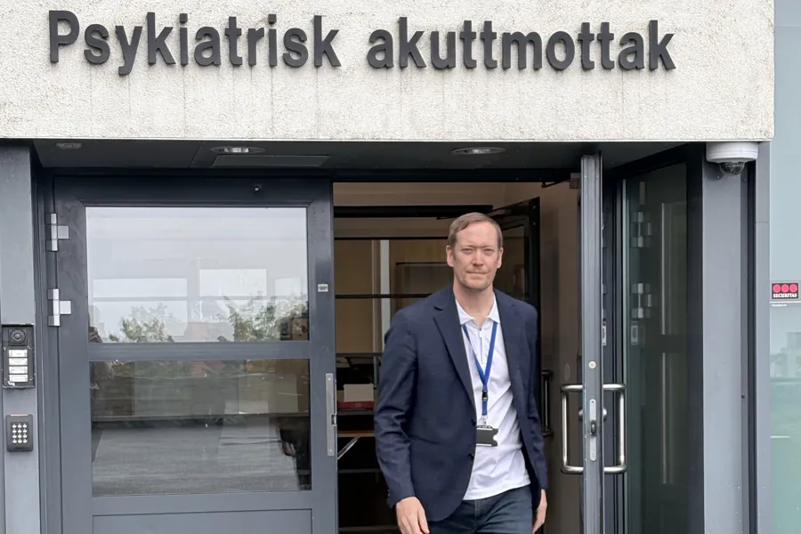 En mann som står ved siden av en inngangsdør som er skiltet med Psykiatrisk klinikk