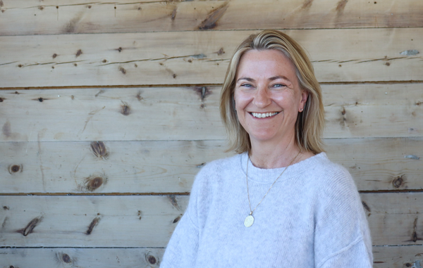 En person som smiler foran en trevegg