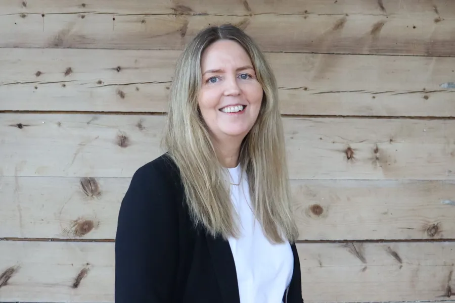 En kvinne med langt hår som smiler foran en trevegg
