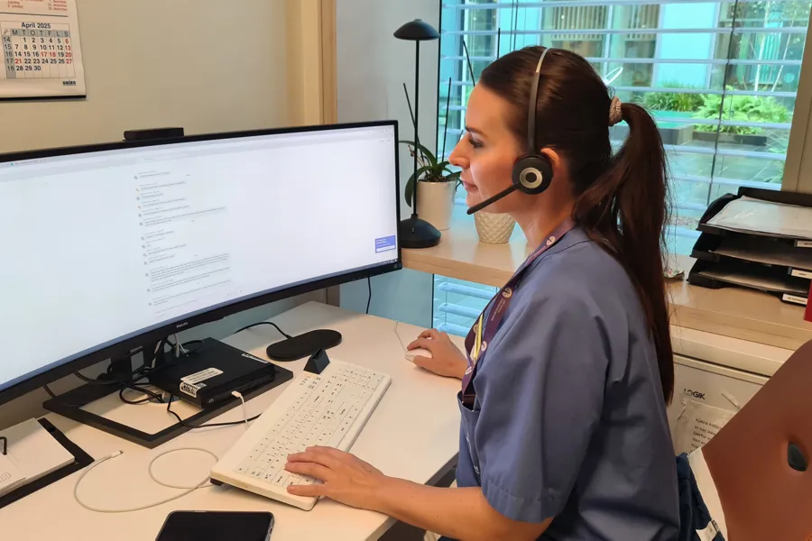 En person som har på seg hodetelefoner og sitter ved et skrivebord med en datamaskin