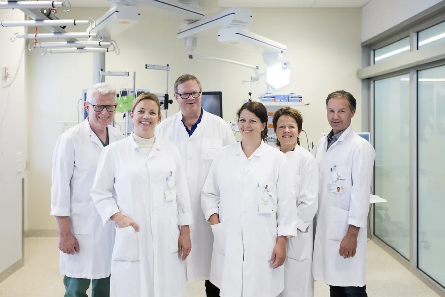 Tre menn og tre kvinner i hvite sykehusfrakker som smiler til kamera