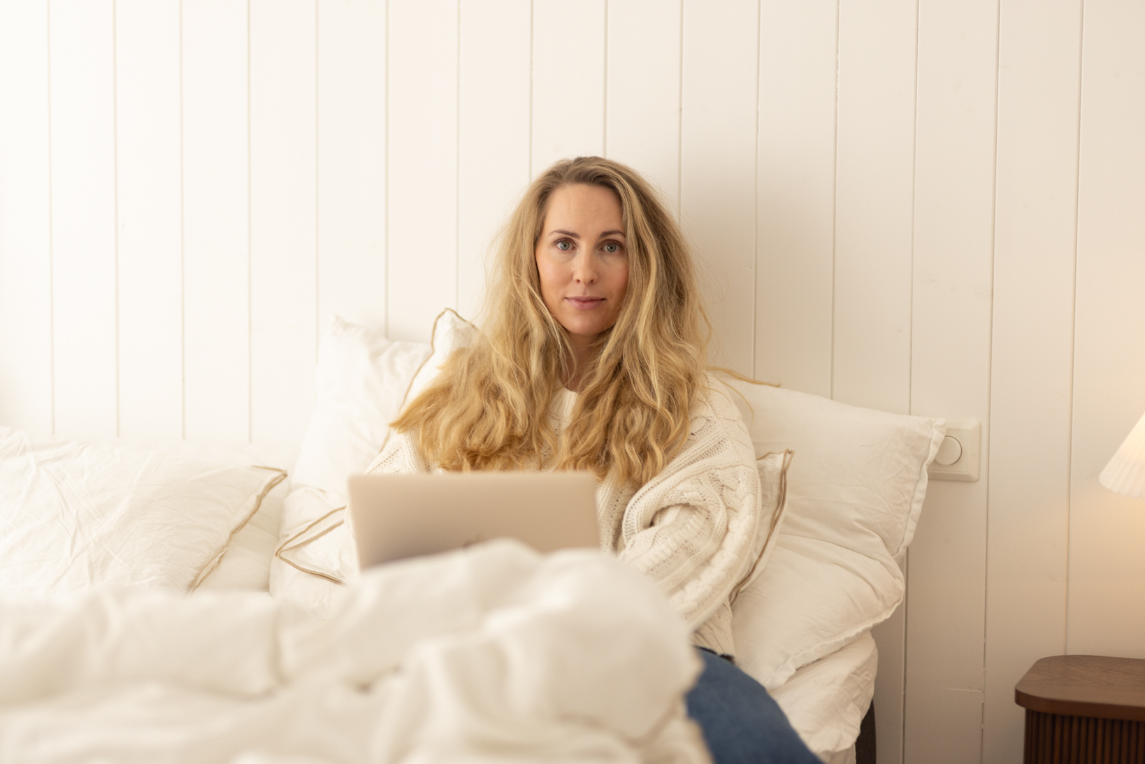 En kvinne som sitter på en seng med en laptop