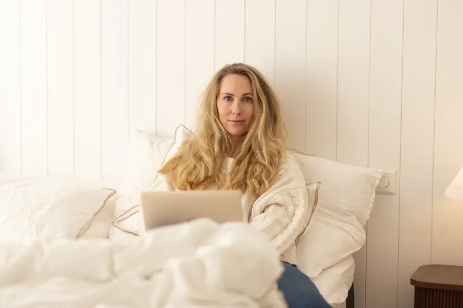 En kvinne som sitter på en seng med en laptop