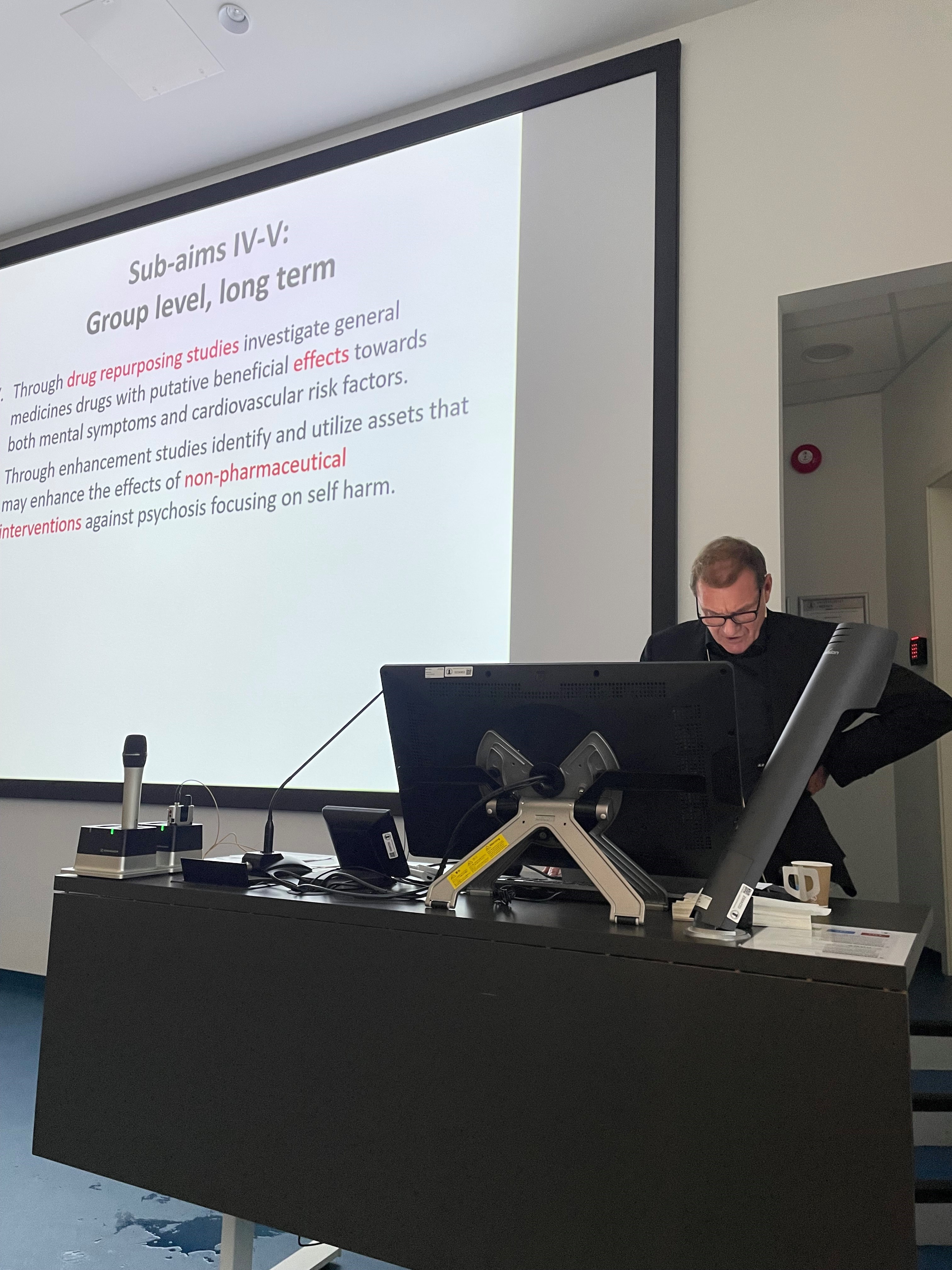 A person sitting at a desk with a computer and a projector screen