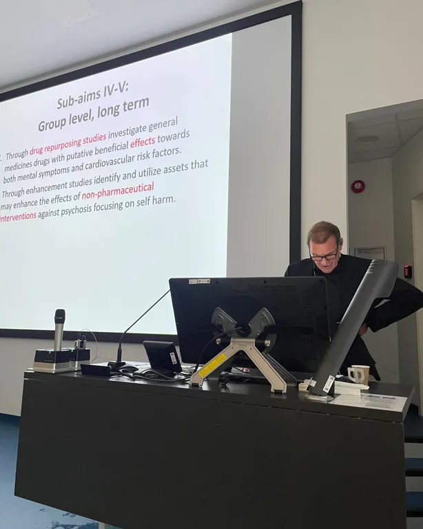 A person sitting at a desk with a computer and a projector screen