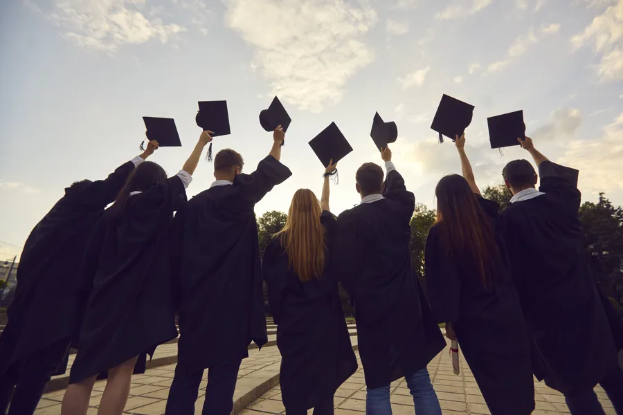 Youth having high hopes. Back view of group of university graduates standing in row holding up black academic caps. Confident college students together tossing hats