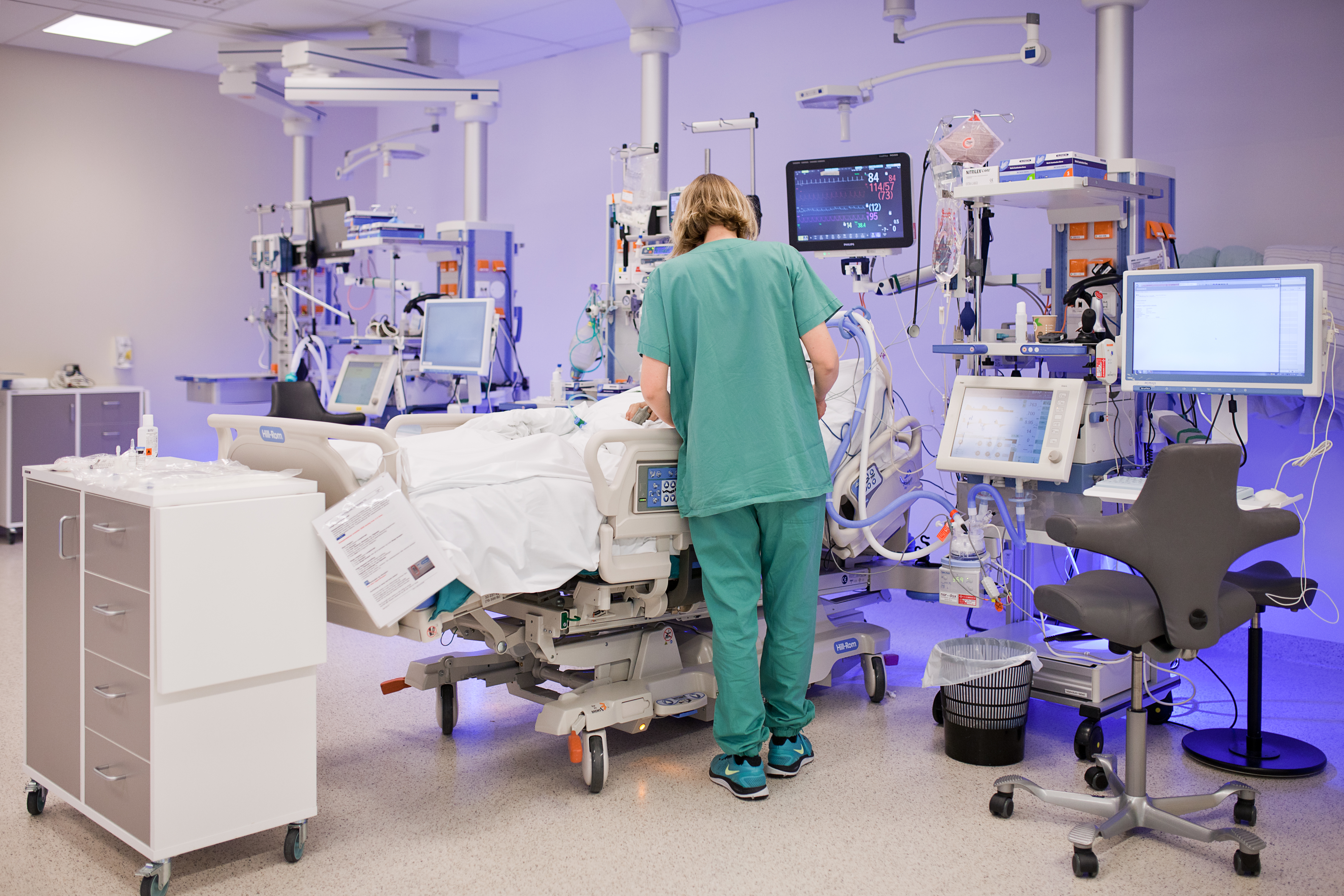 Person i grønt antrekk står ved en syksehusseng