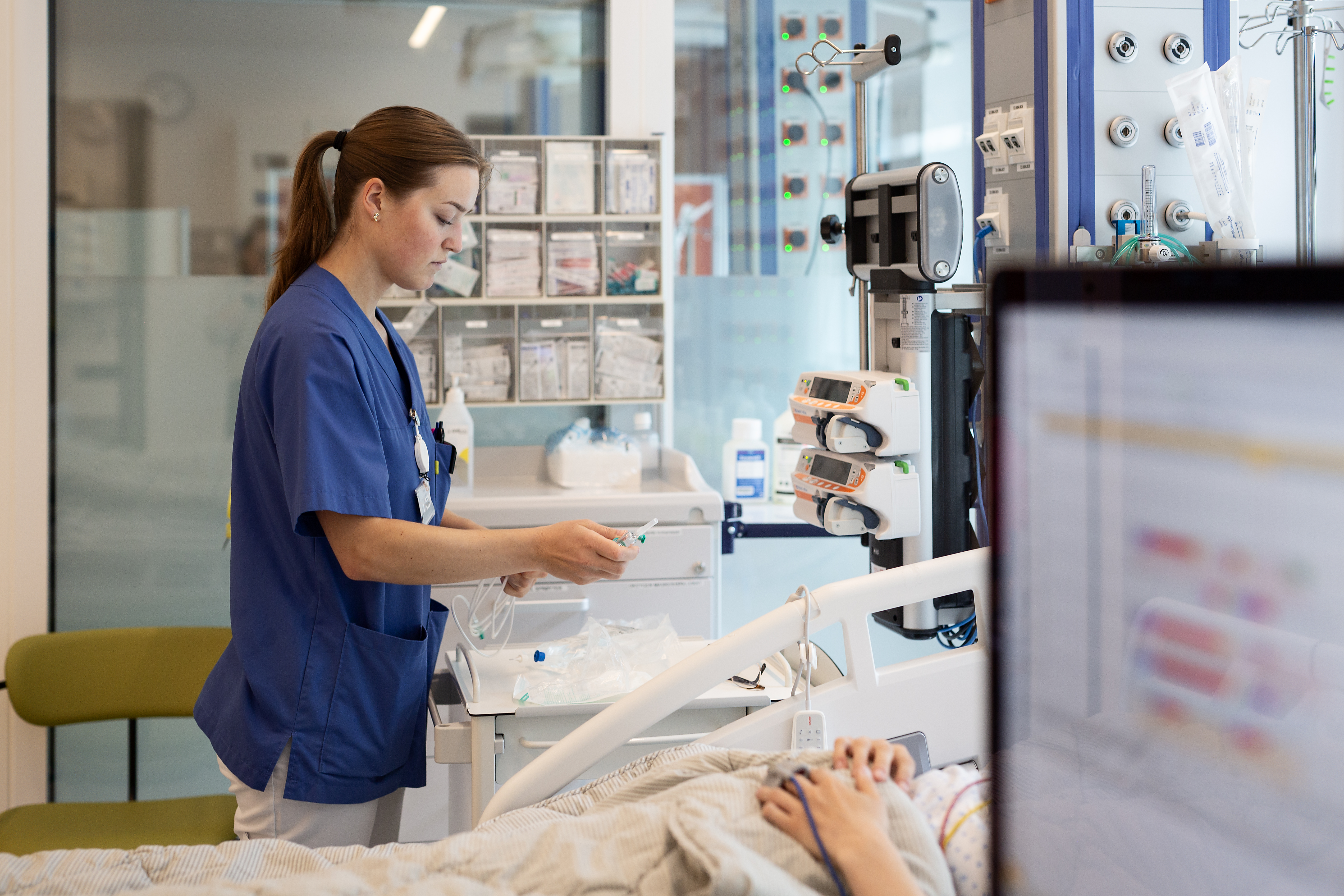 Sykepleier står ved en seng med pasient