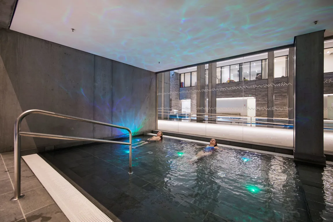 Et par mennesker i et svømmebasseng med en bygning i bakgrunnen