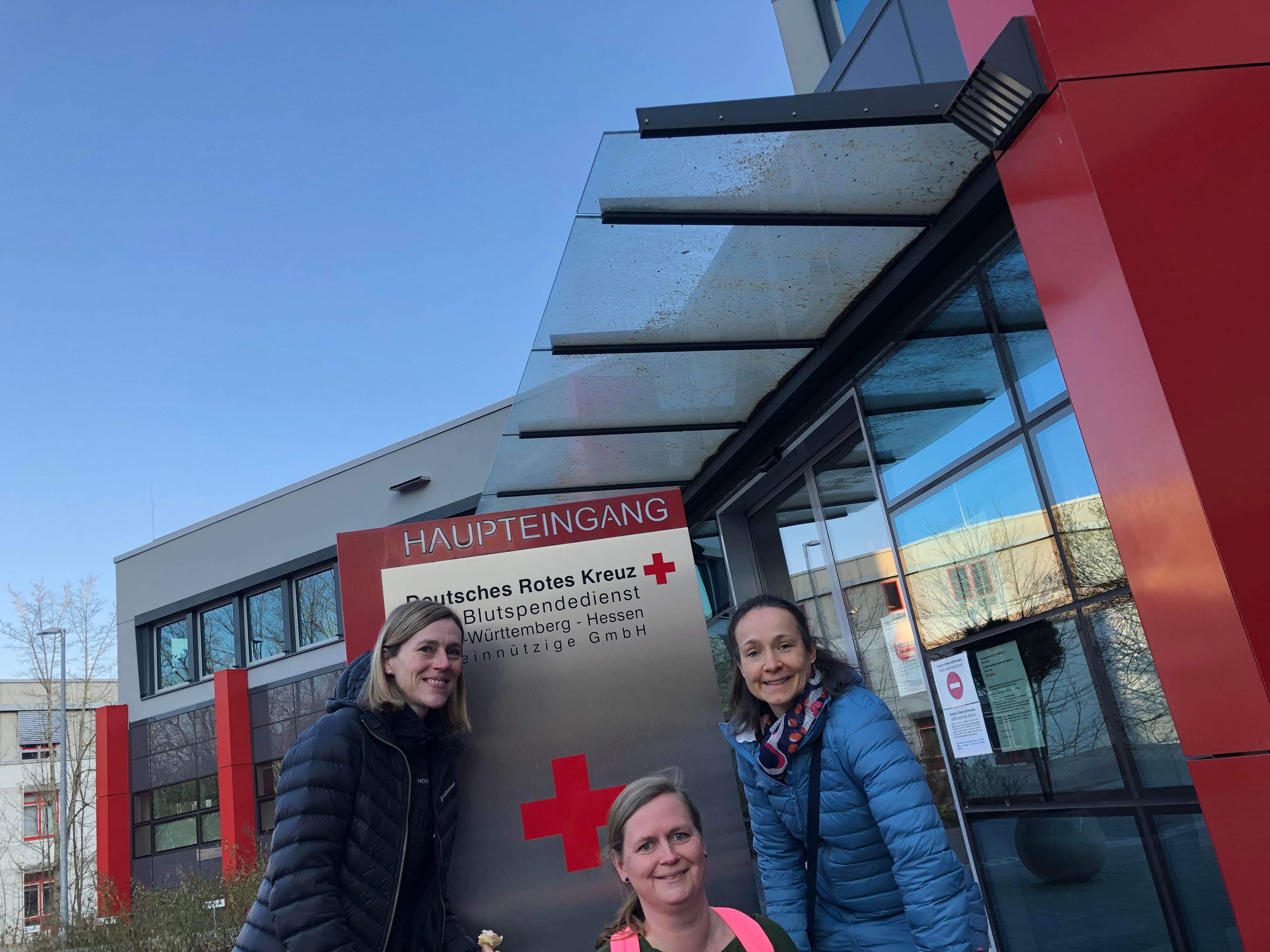 Three persons in front of Red Cross sign. Photo