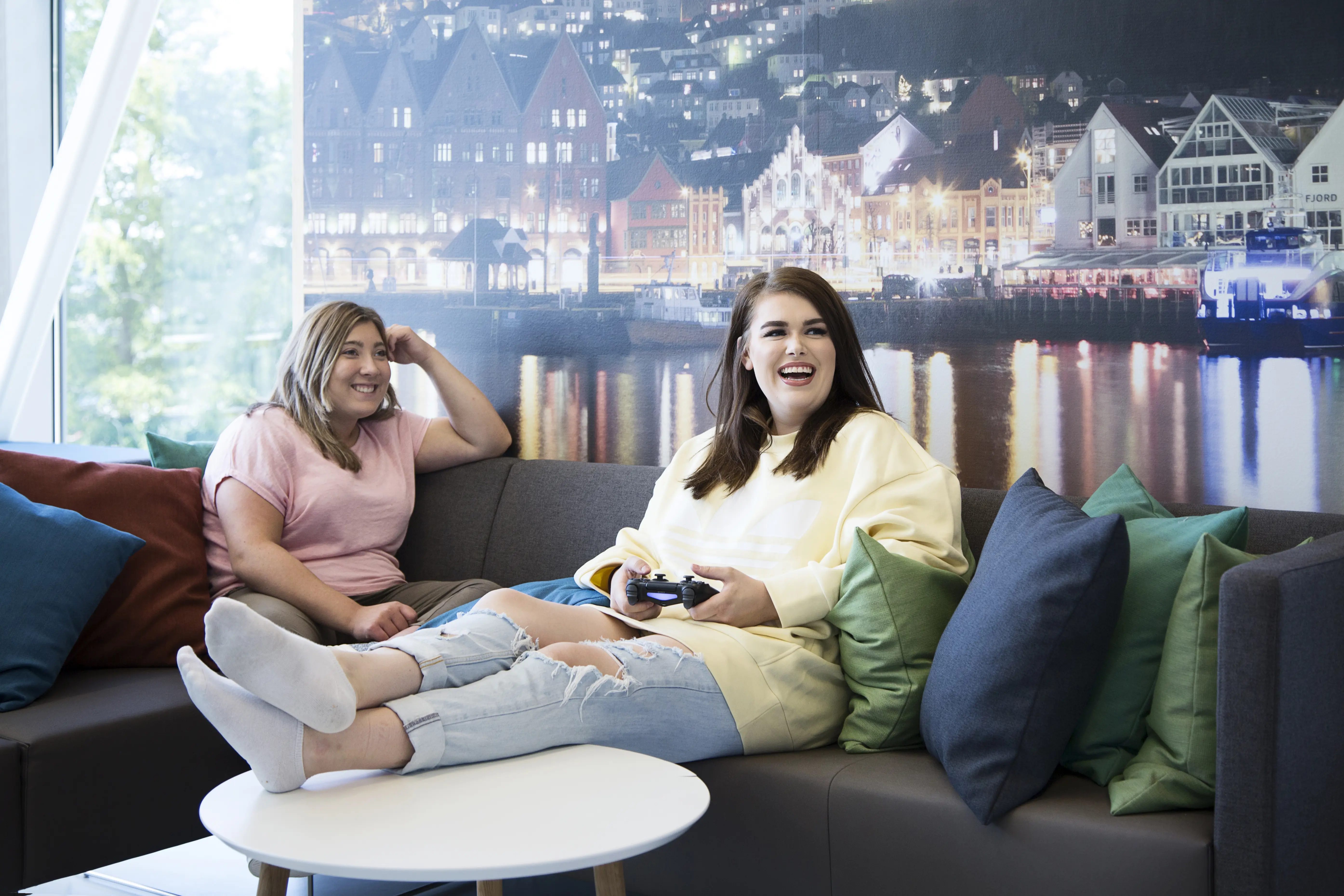 To unge jenter sitter i sofa og spiller dataspill. Foto