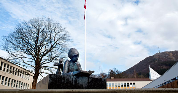 En statue av en mann og en kvinne som sitter på en stein foran en flaggstang og