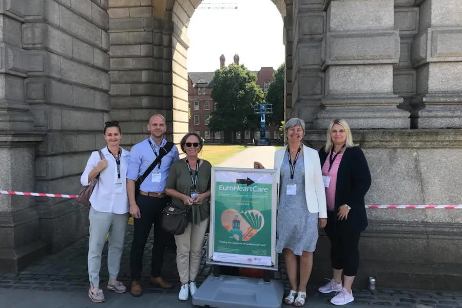 Gruppebilde forskningsgruppe med fem personer står ved skilt med informasjon om forskningskonferanse. Foto