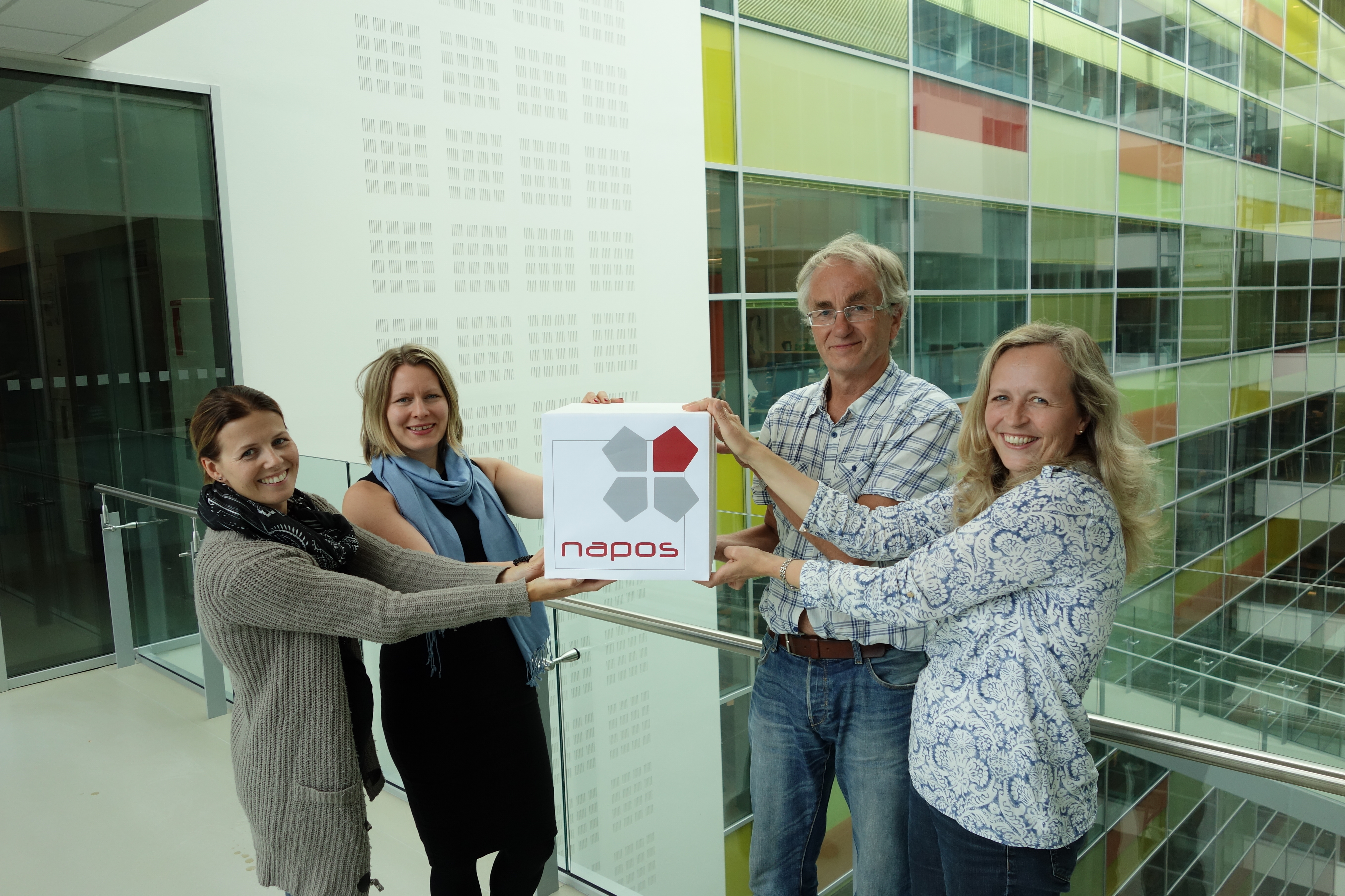 Fire ansatte ved NAPOS holder en boks med logo