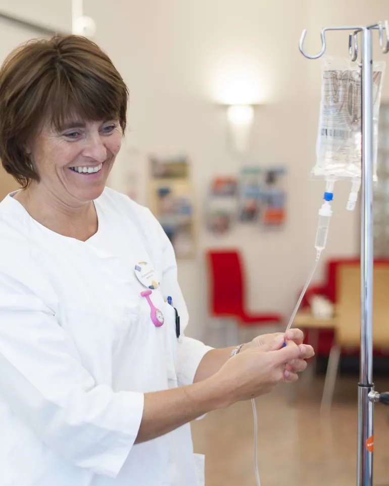 Smilende sykepleier med dryppstativ. Foto