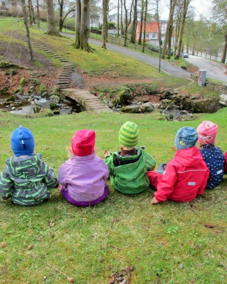 gruppebilde barn sitter på gressplen med ryggen til. Foto