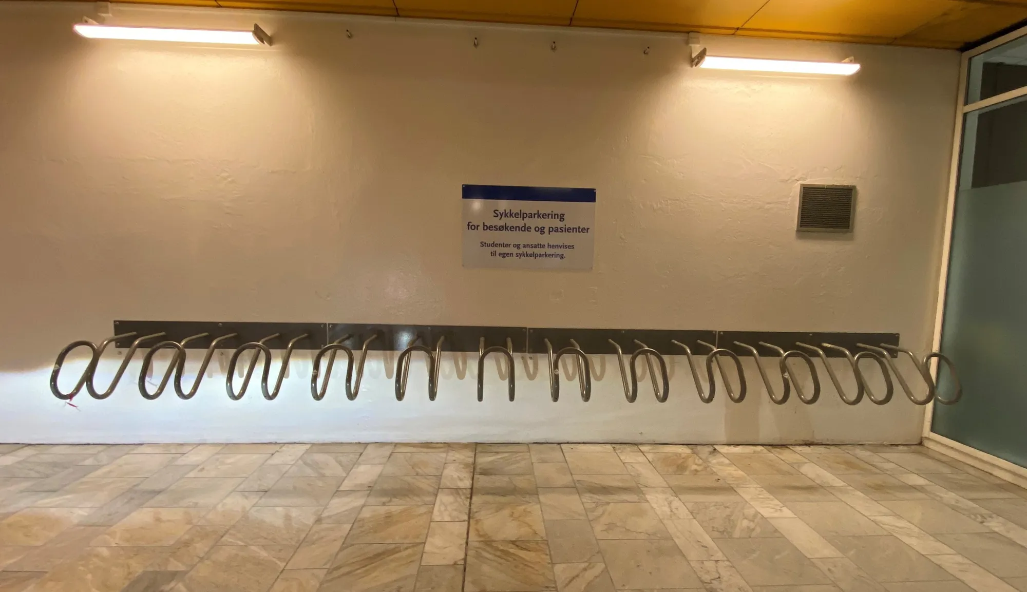 Sykkelparkering og stativ på murvegg. Foto