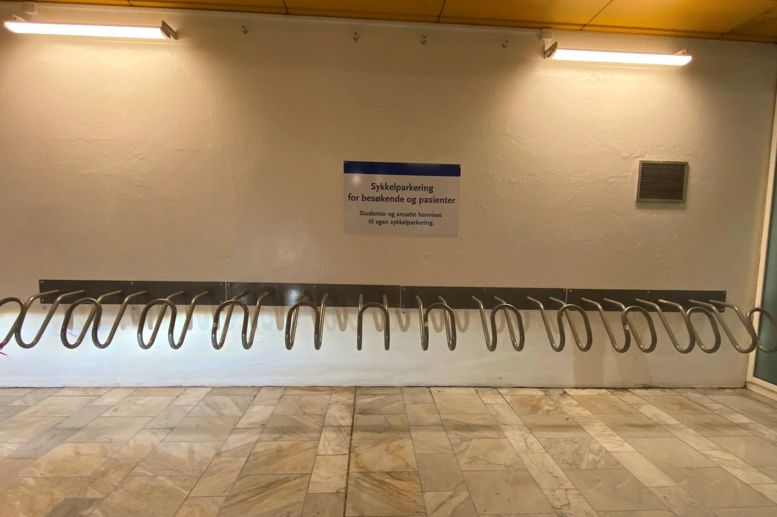 Sykkelparkering og stativ på murvegg. Foto