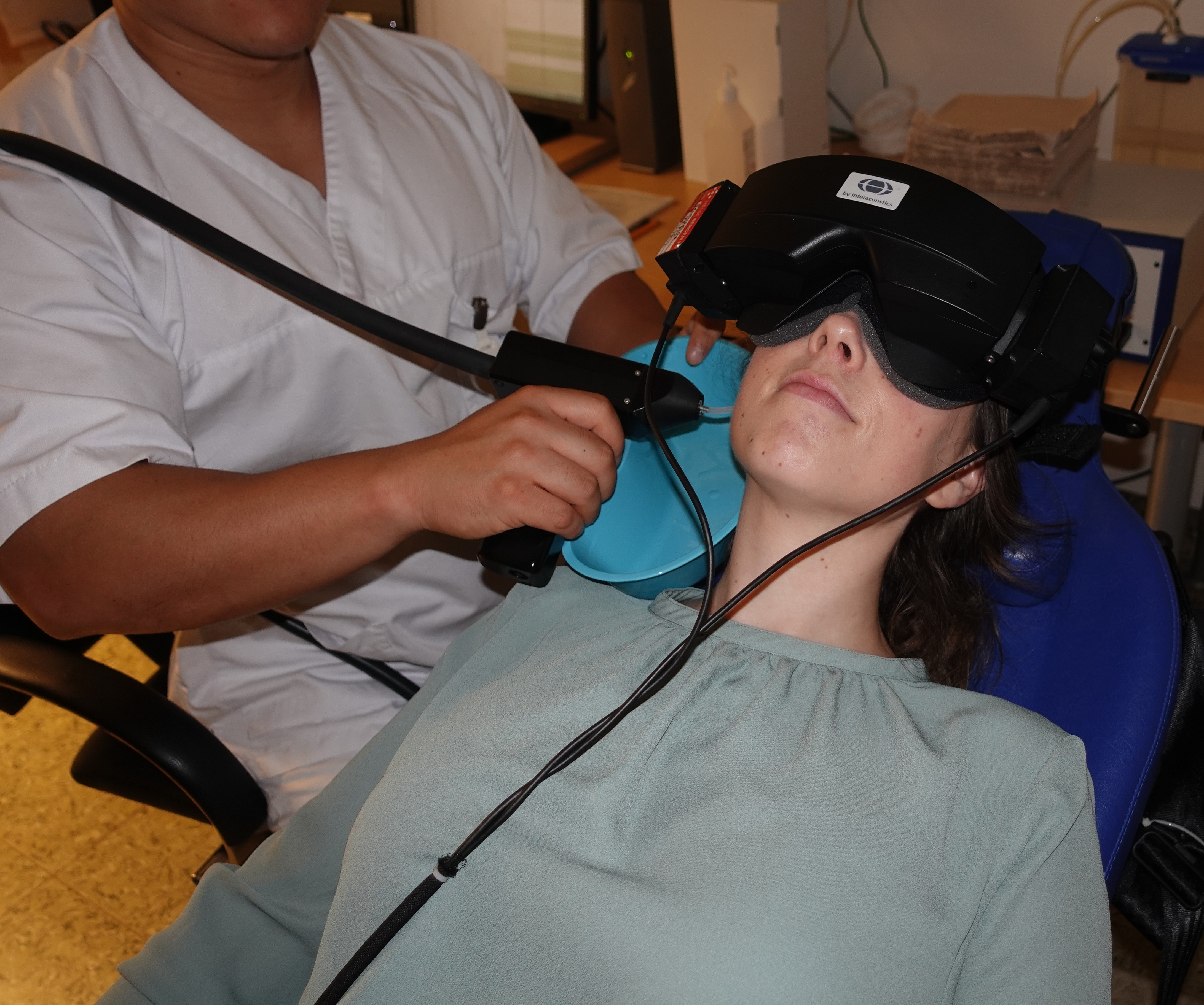 Helsepersonell undersøker kvinnelig pasient som ligger med videobriller på seg. Foto