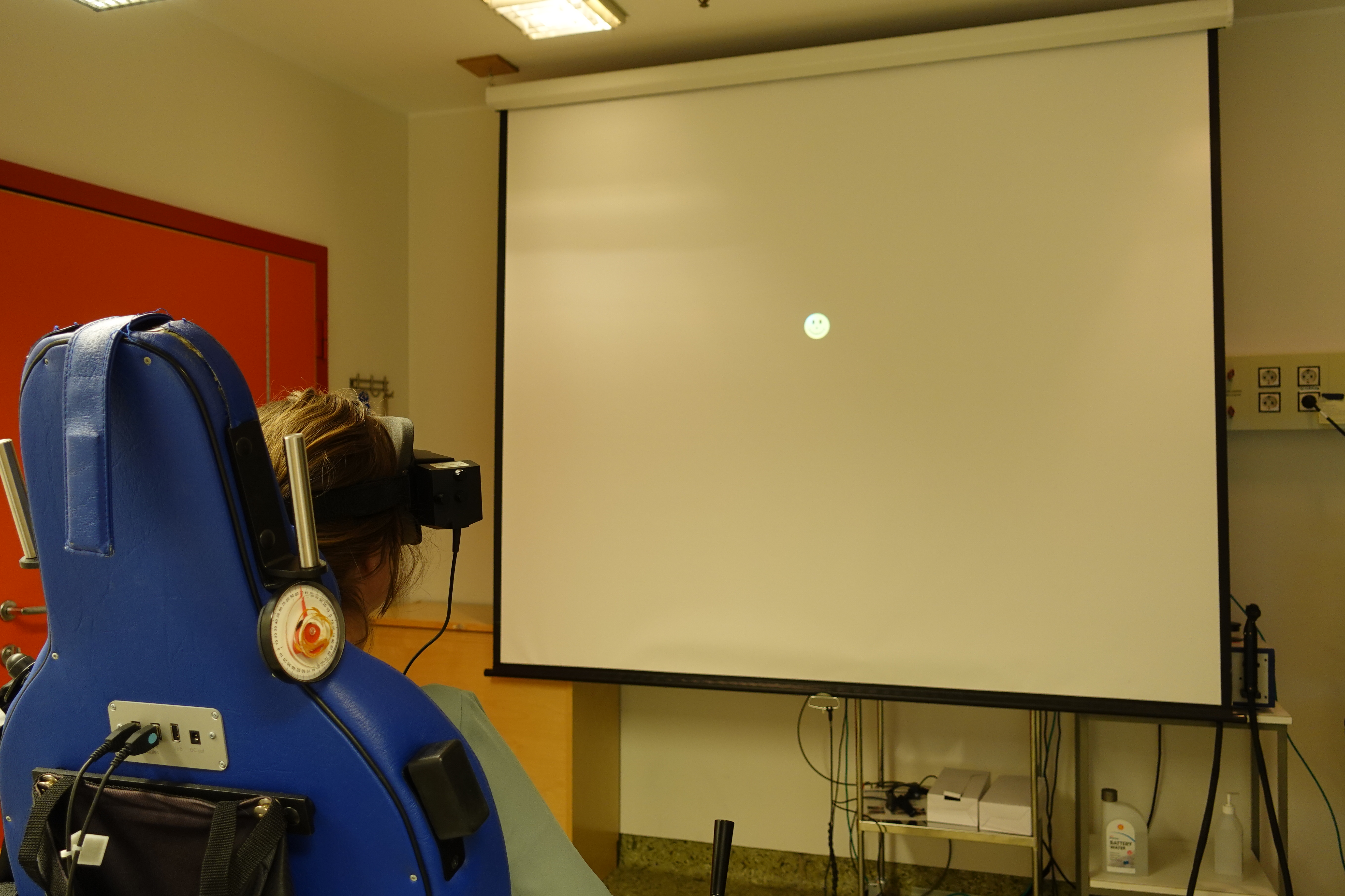 Pasient sitter i stol med videobriller og ser mot lerret. Foto