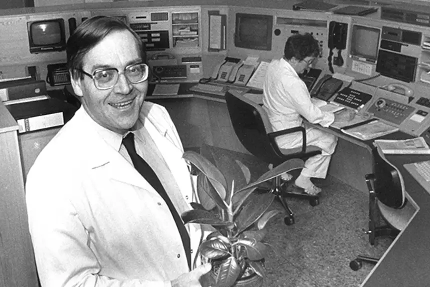 Mann i hvit frakk med potteplante i sentralrom. Foto