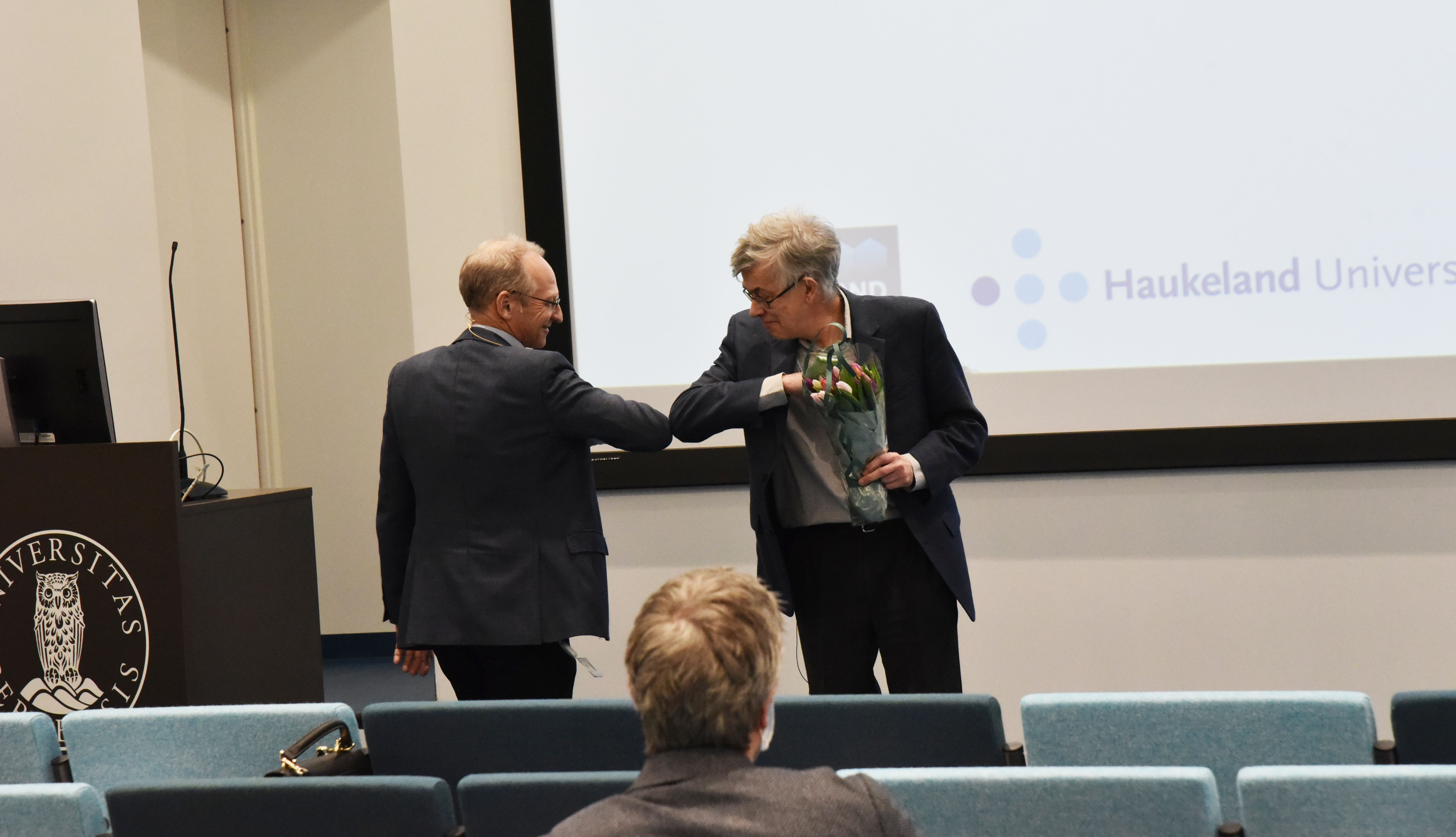 Foredragsholder hilser med albuen. Foto