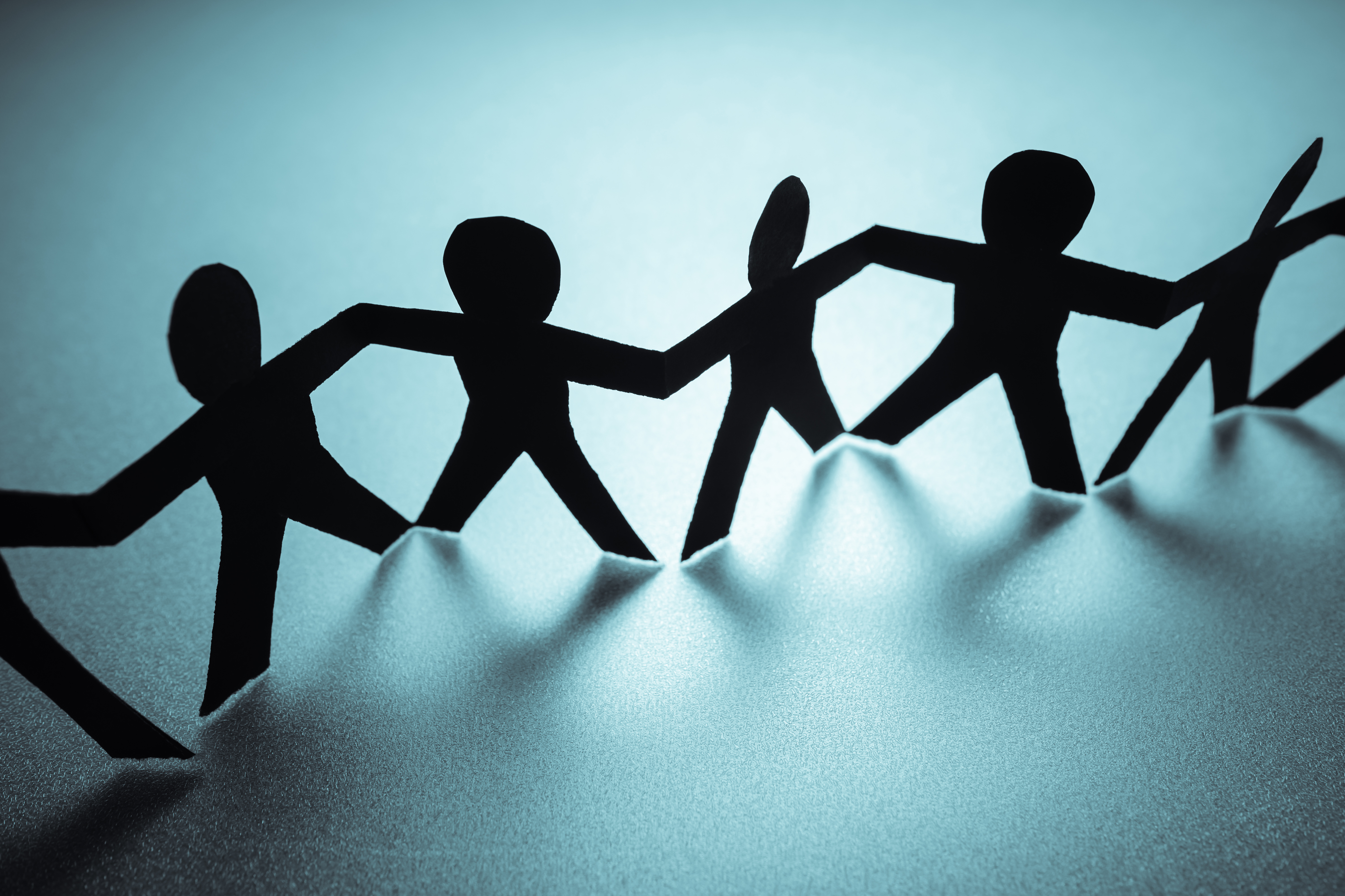 Papirmenneskefigurer i svart på rekke mot blå bakgrunn. Illustrasjonsfoto