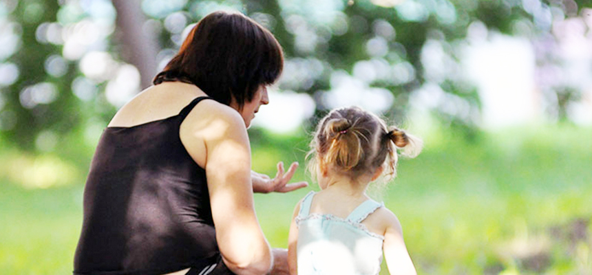 Voksen dame og barn sitter på benk med ryggen til.