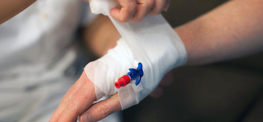 Sjukepleiar tar støttebandasje på hand med venflon. Foto
