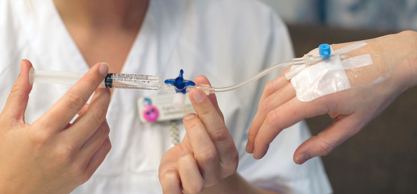 Sykepleier setter inn saltvann i venflon. Foto​