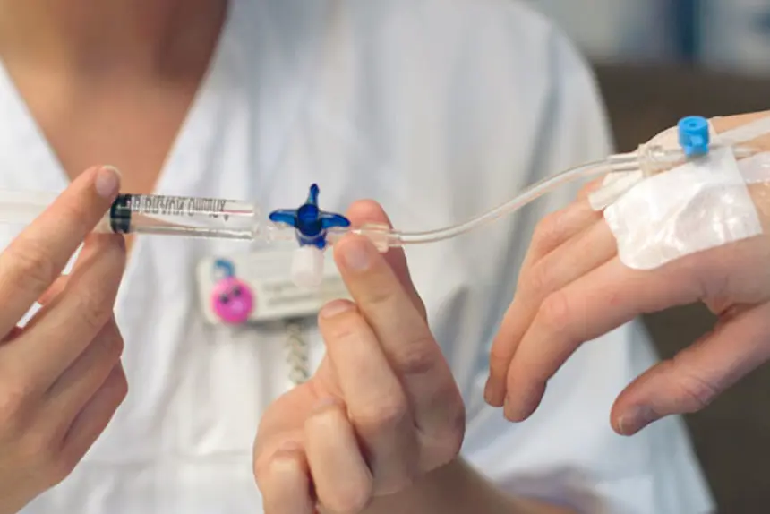 Sykepleier setter inn saltvann i venflon. Foto