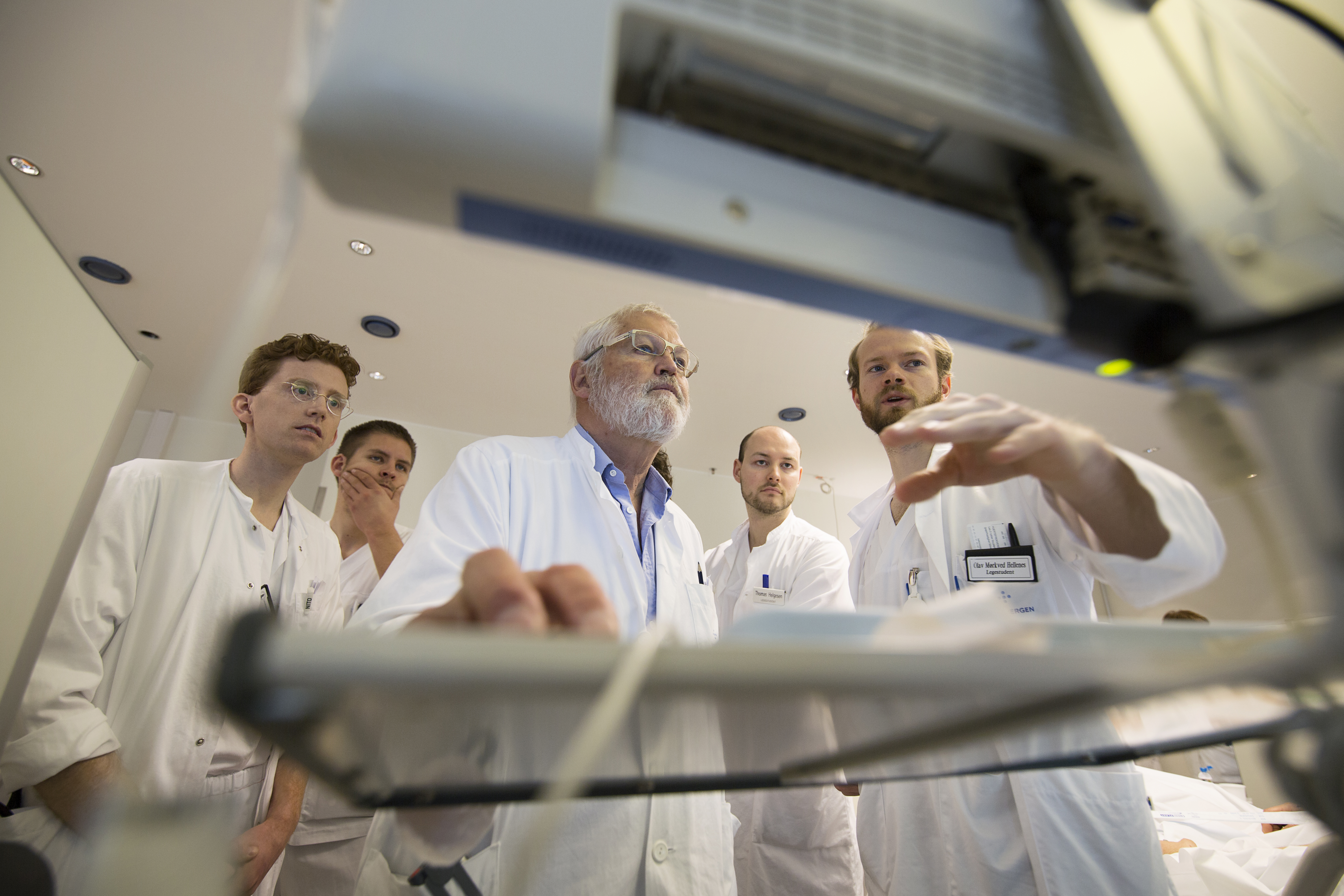Undervisning for gruppe medisinerstudenter i uniform som står samlet rundt skjerm og medisinsk-teknisk utstyr. Foto