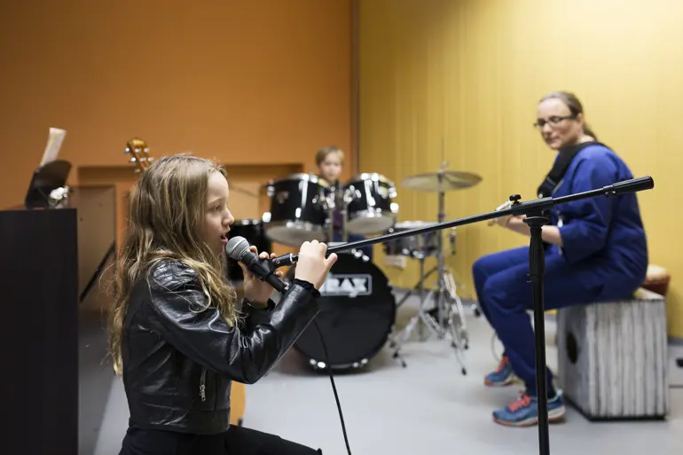jente synger i mikrofon og musikkterapeut spiller gitar