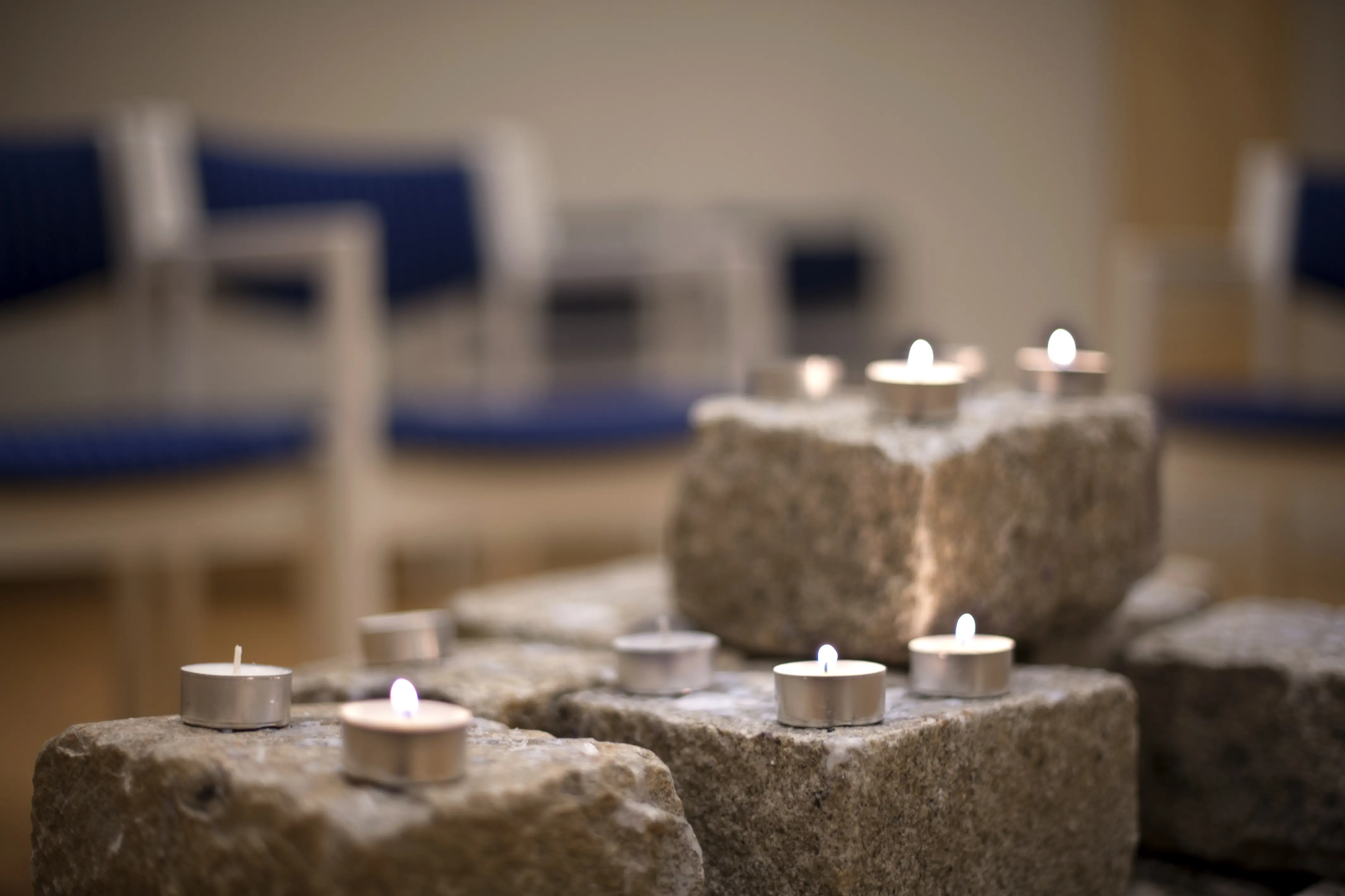 Lit candles on stone bricks and chairs in the background. Photo