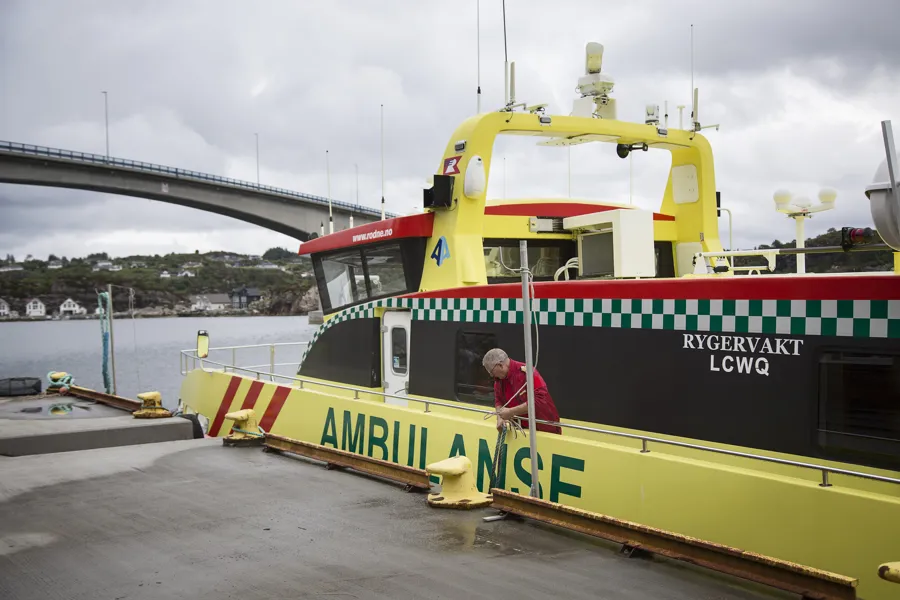 Ambulansebåt ligg til kai i Austevoll med bro i bakgrunnen. Foto