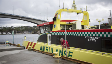 Ambulansebåt ligg til kai i Austevoll med bro i bakgrunnen. Foto