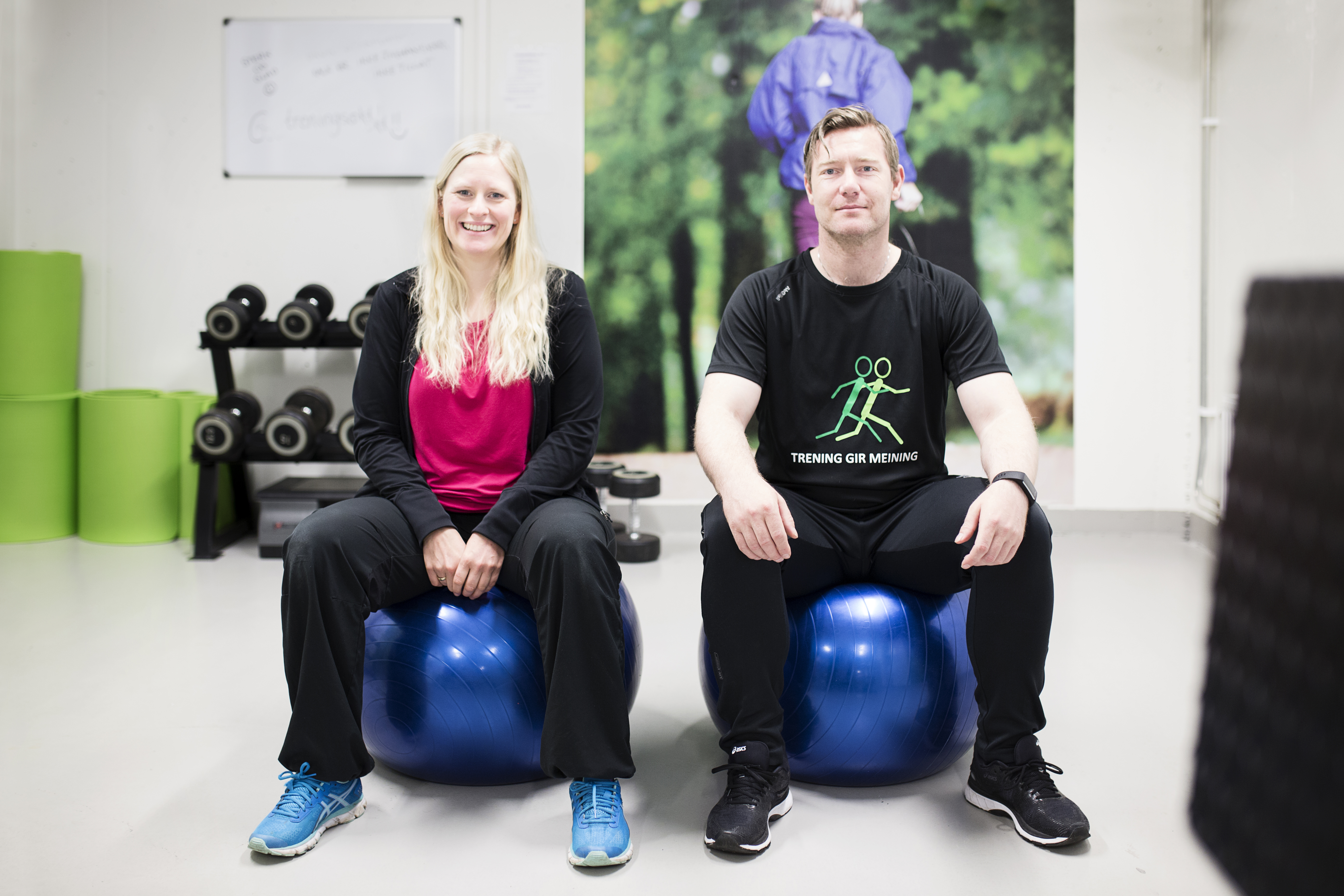 Kvinne og mann i treningsklær sitter på hver sin blå treningsball. Foto