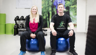 Kvinne og mann i treningsklær sitter på hver sin blå treningsball. Foto