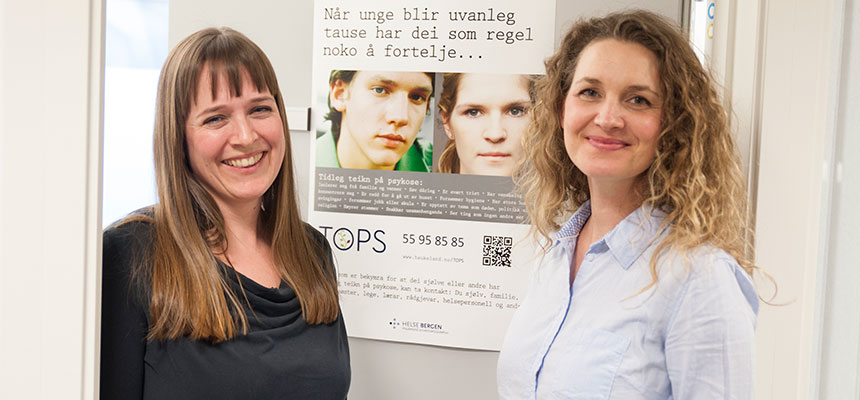 To kvinnelige tilsette foran Tops-plakat. Foto