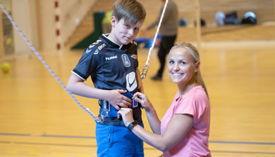 Sykepleier fester sikkerhetsutstyr på ung gutt i gymsal. Foto