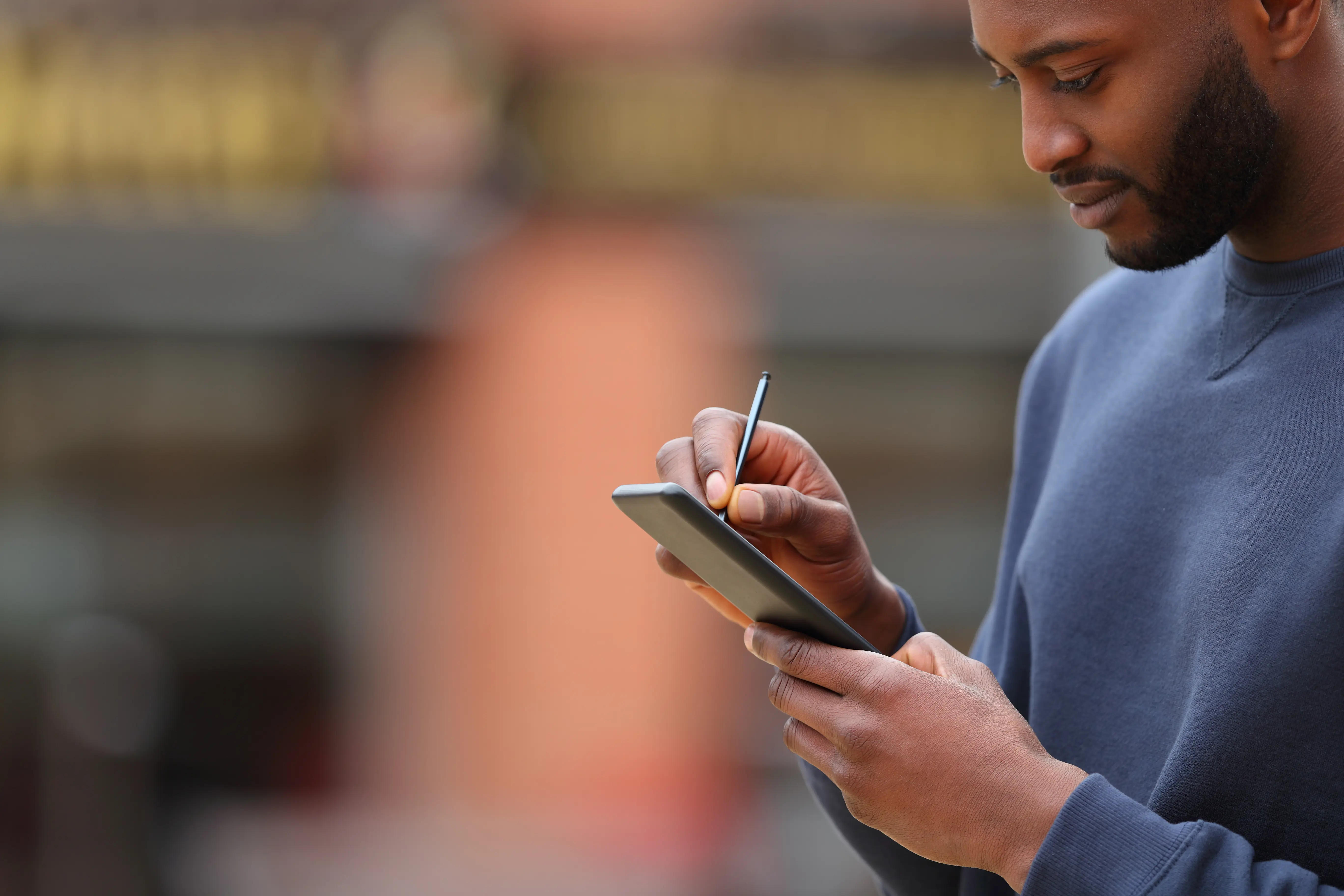 Melaninrik mann i grå genser trykker på smarttelefonen sin. Foto