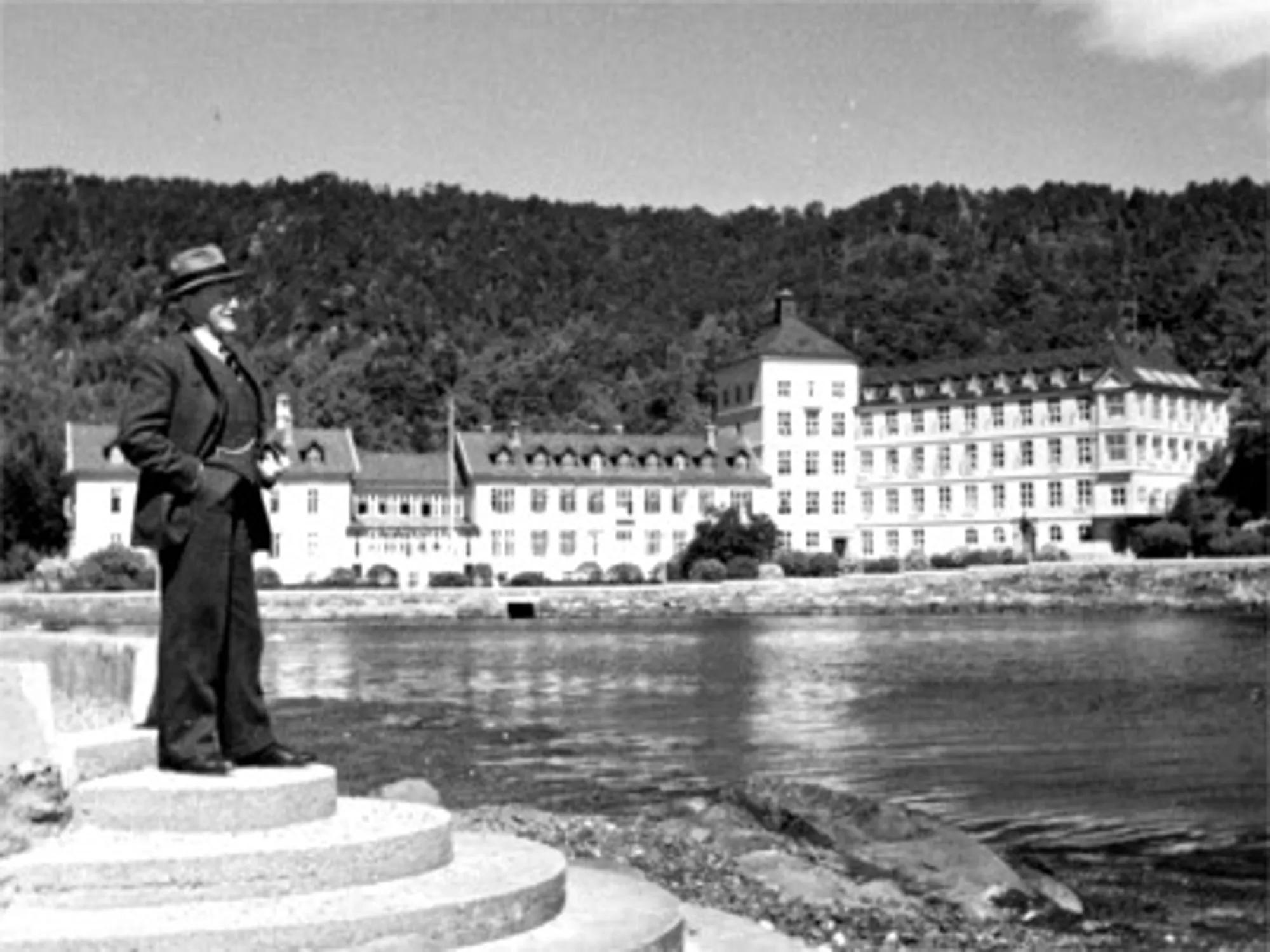 Herman G. Gade står i profil ved vannet med Kysthospitalet i Hagevik i bakgrunnen i 1936. Foto