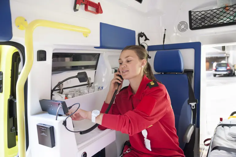 Ambulansearbeider snakker i telefonen inni ambulansen. Foto.