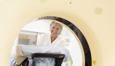Kvinnelig helsepersonell kledd i hvitt smiler og ser gjennom ct trommel. Foto