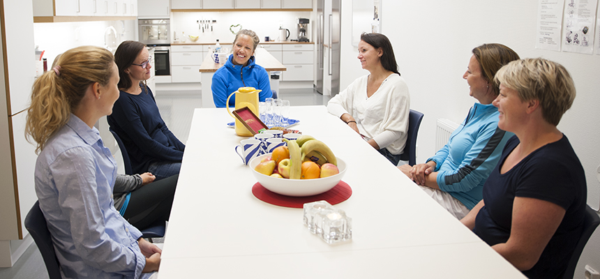 Gruppesamtale. Seks kvinner sitter rundt møtebord med kaffe og frukt. Foto.