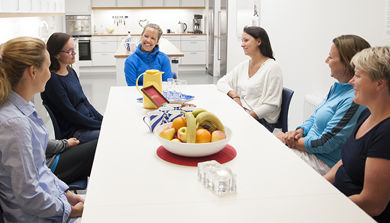 Gruppesamtale. Seks kvinner sitter rundt møtebord med kaffe og frukt. Foto.