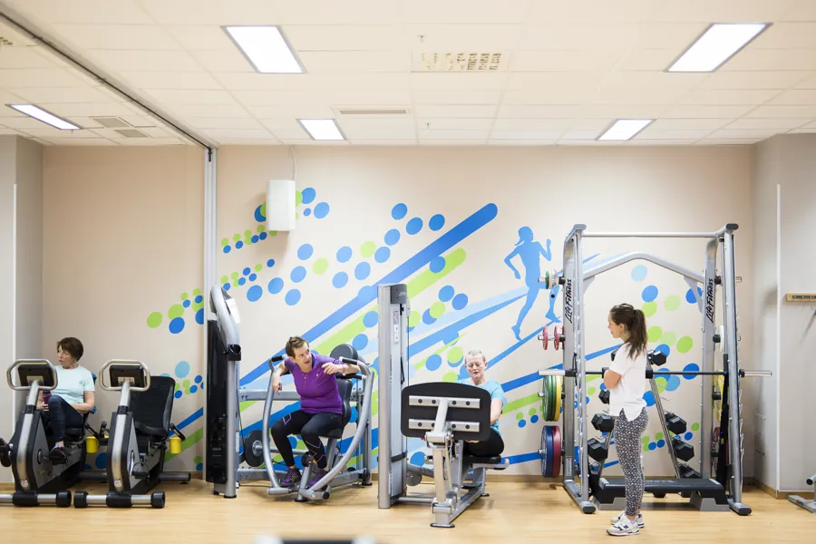 Tre kvinner trener på ulike treningsapparat med veiledning fra kvinnelig instruktør i treningsrom. Foto